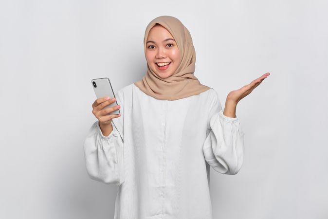 Asian female in headscarf gesturing maybe and holding cell phone