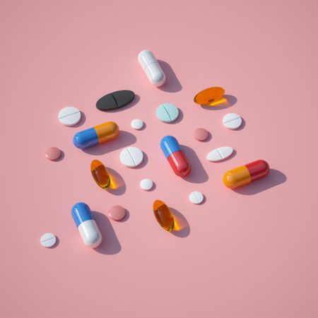 Pills and capsules on pink background with summer sun and sharp shadow
