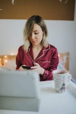 Woman sitting in bed with tablet and looking on smartphone