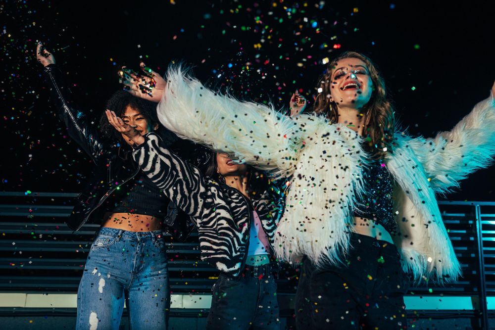 Multi-ethnic group of female friends celebrating with confetti on terrace