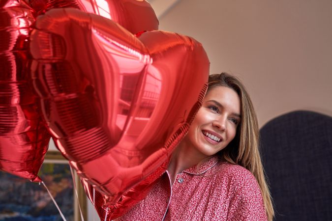 Cheerful woman with bouquet of red heart foil balloons