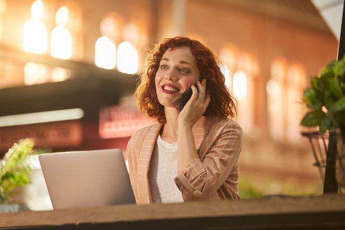 Young woman talking on phone while working on laptop