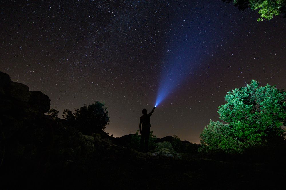 Person illuminating star with flashlight on hill
