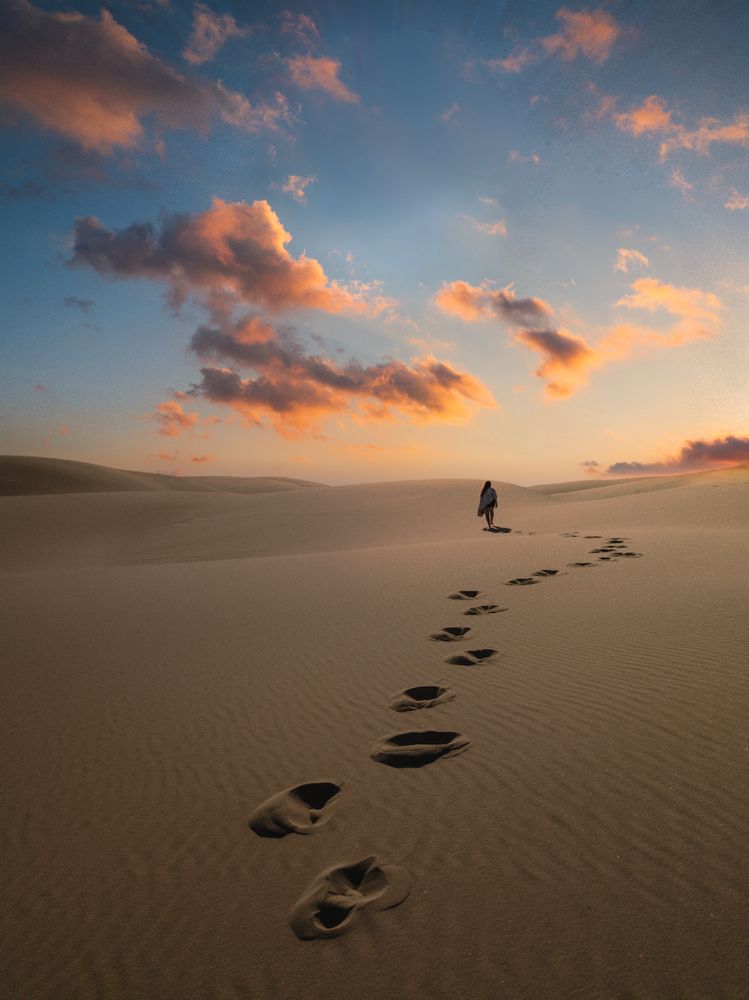 Foot steps on sand by a person walking in desert at sunset