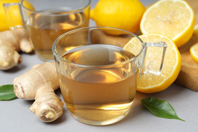 Cups of tea, ginger and lemons on gray background, close up