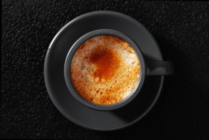 Top view of cappuccino in dark cup and saucer