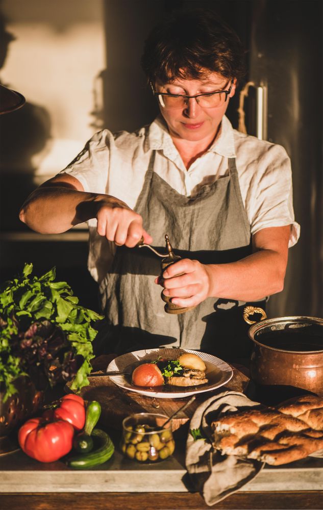 Woman in gray apron grinder pepper onto stew
