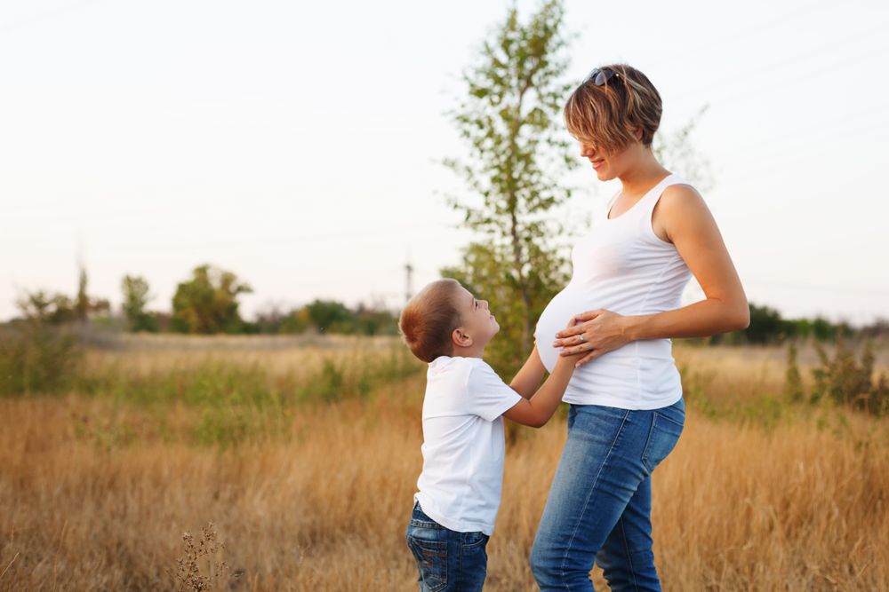 Pregnant mother and her son standing facing each other in nature