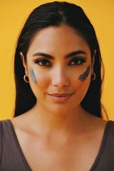 Smiling Latina woman standing with mud mask on face, vertical
