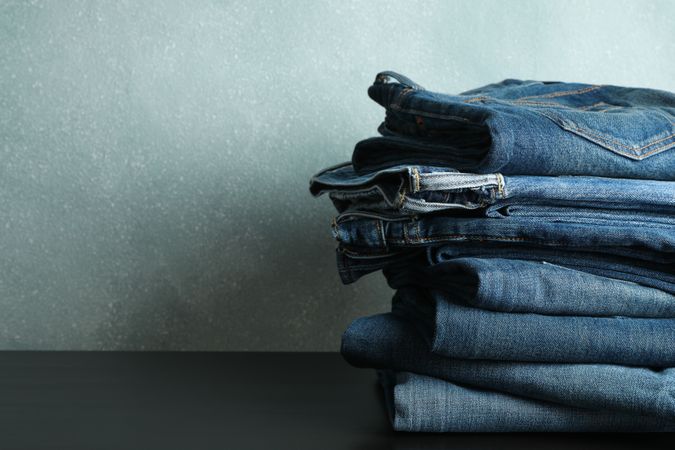 Stack of jeans pants on table, space for text