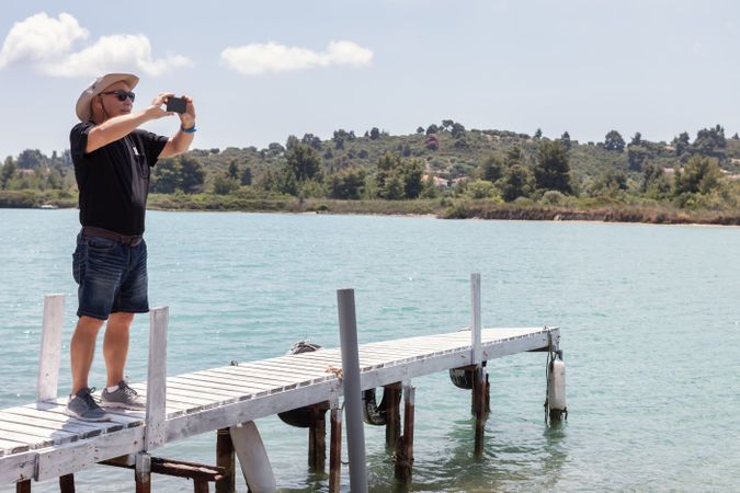 Man standing on dock and taking photo of landscape