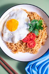 A plate of noodles with an egg and tomato on top