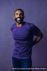 Happy male in purple studio with arms behind his back, vertical 5kA8jb