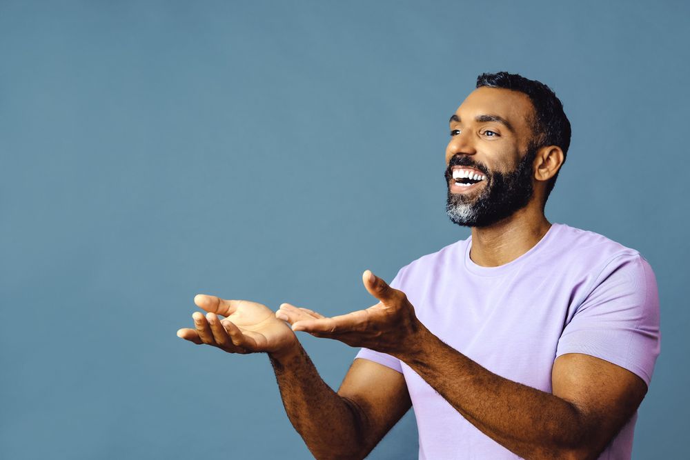 Male speaking in purple t-shirt with hands open to copy space