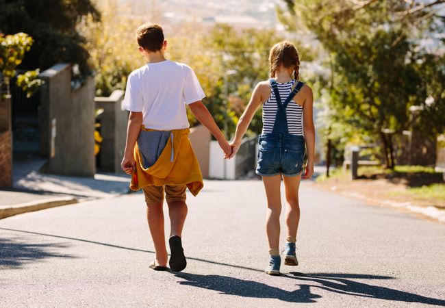 Full length of boy and girl walking on an empty road together holding hands