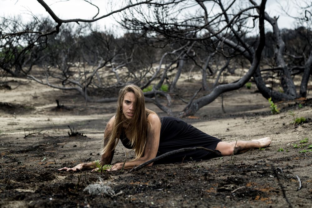Woman posing on ground near dry trees