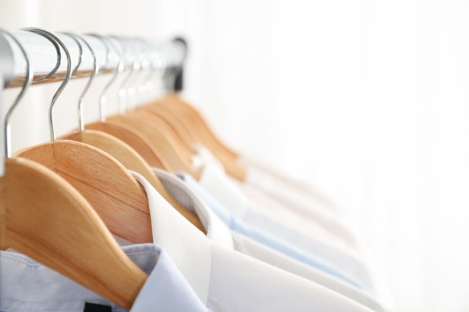 Hangers with shirts against light background, copy space