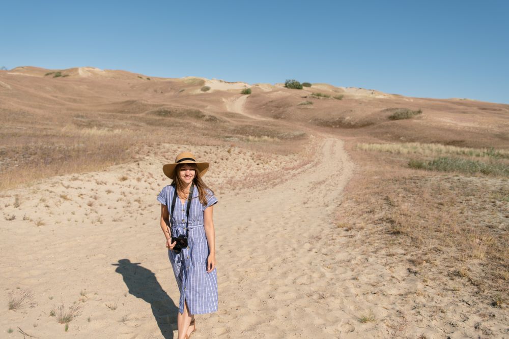 adult woman in straw hat and dress with camera walking on country path