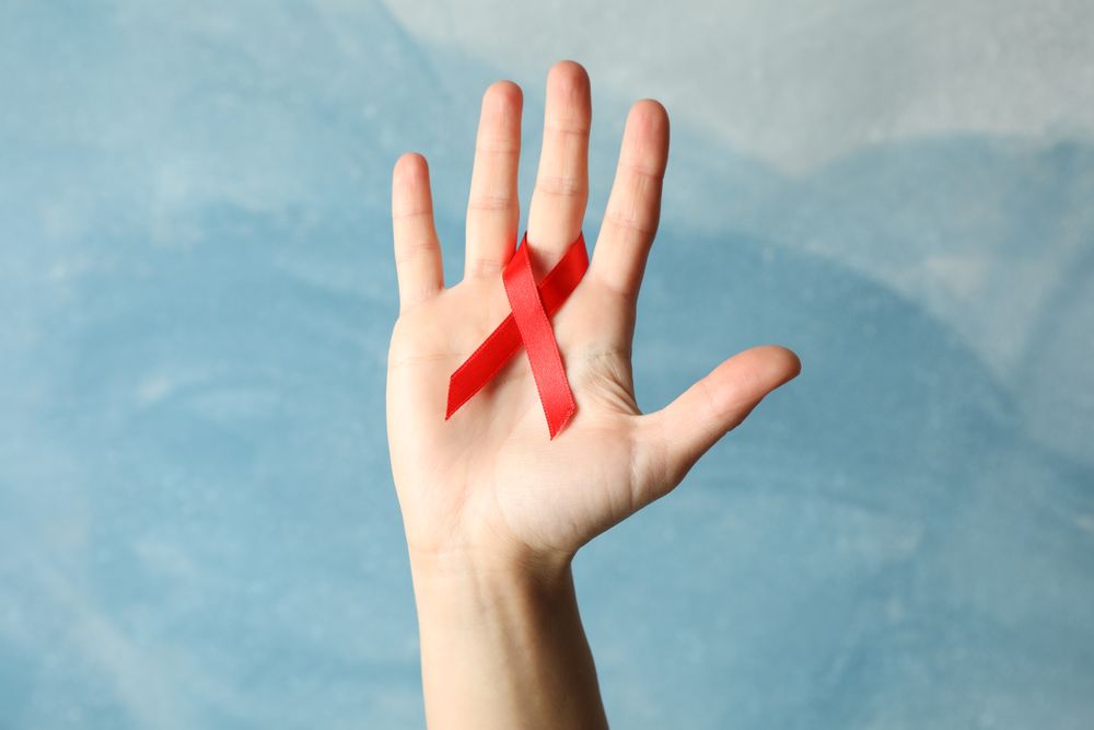 Hand and red awareness ribbon against blue background, space for text