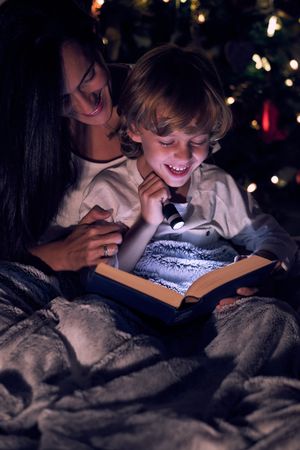 Smiling mother with son reading book in darkness
