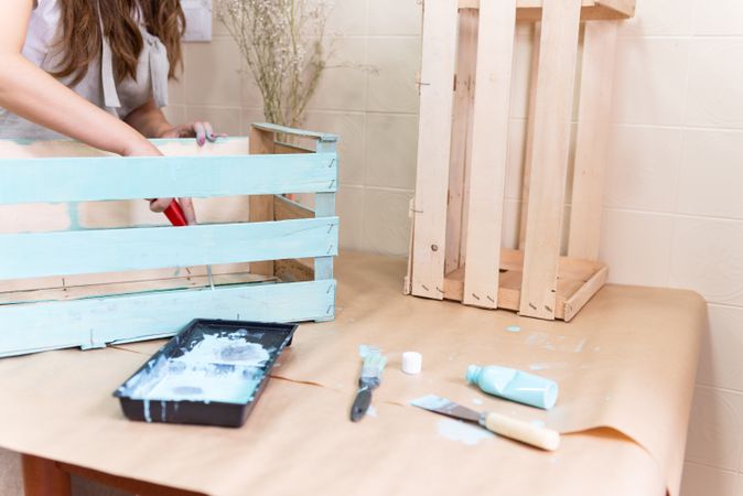 Woman paining wooden box in blue color with roller