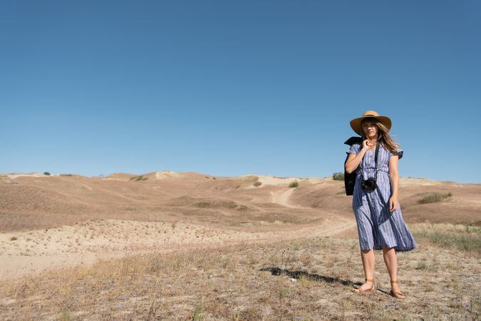adult woman in straw hat and dress with camera standing on country path