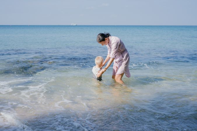Woman and small kid having fun with water while relaxing on seacoast at resort