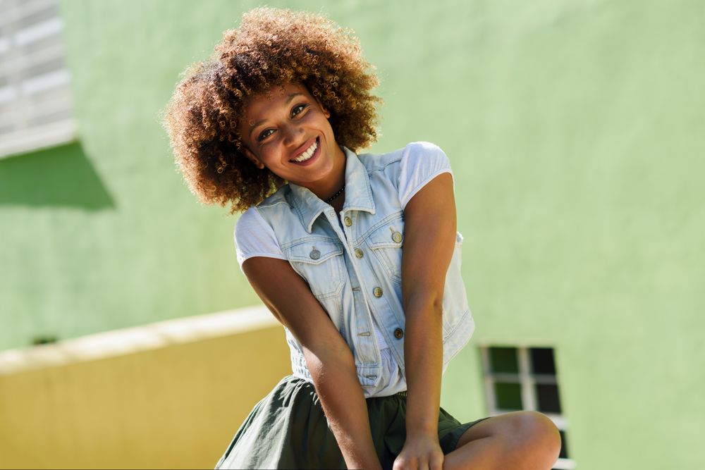 Smiling woman denim shirt sitting in front of green wall