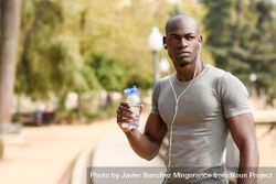 Fit male drinking from a water bottle in an outdoor park 0JaEnb