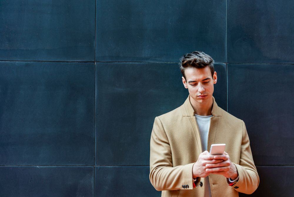 Man texting while leaning against dark wall