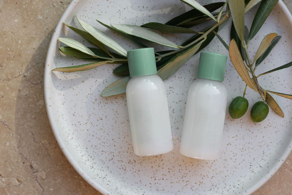 Summer cosmetic still life; shampoo or cream bottles with green cap next to olive tree branch