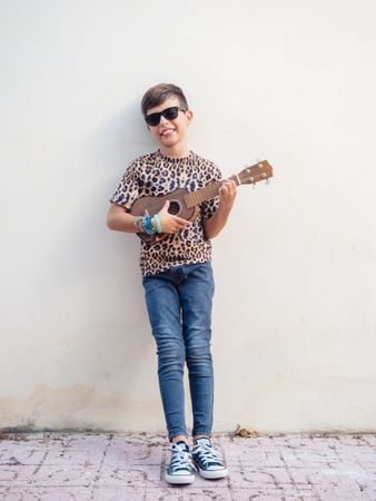 Excited kid raising hands up with ukulele