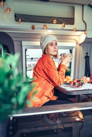 Vertical composition of woman sipping coffee in back of camper van