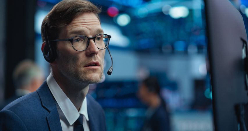 Adult Man in Glasses Looking at Computer Screen, Communicating with a Client on a Phone Call, Talking About a Buying Strategy