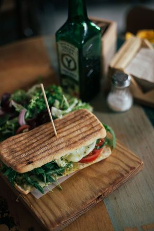 Grilled sandwich on rustic wooden board in cafe with bottle of olive oil