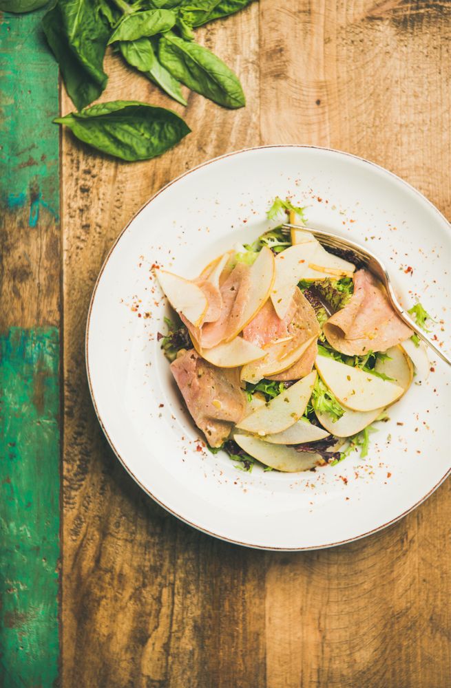 Top view of ham and pear in bowl, on green trimmed wooden background