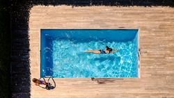 Woman swimming in outdoor pool near son standing on wooden deck