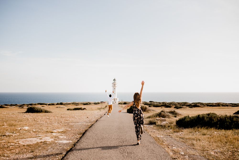 Happy lovers jumping with arms raised on path to lighthouse
