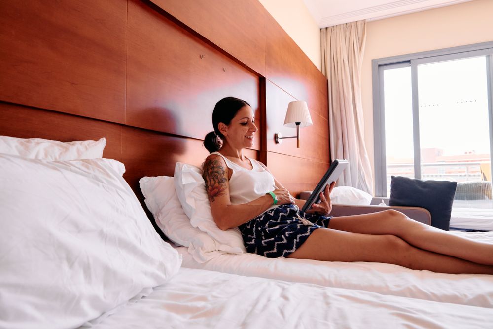 a young woman lying on a hotel bed using a digital tablet