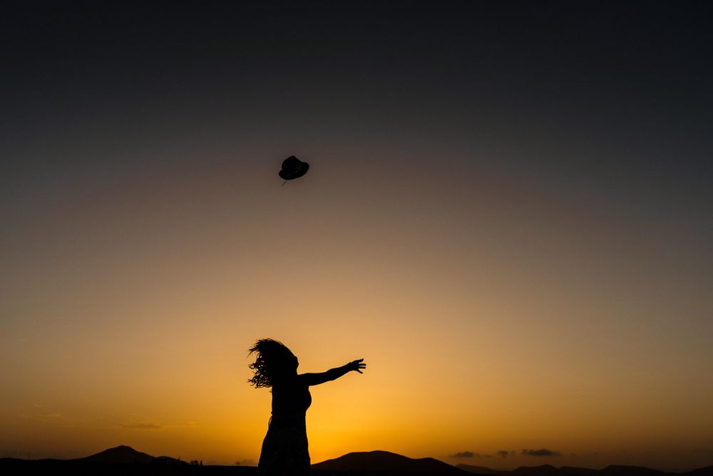 Woman throwing hat into distance to sun
