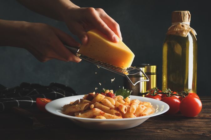 Woman grating cheese on pasta. Cooking pasta composition