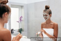 Happy young woman applying face mask in bathroom and smiling 42oBmb