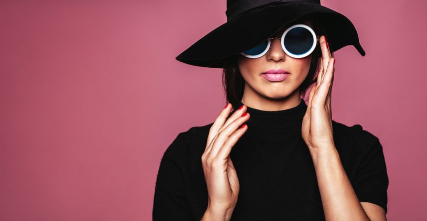 Beautiful woman in hat and sunglasses posing over pink background
