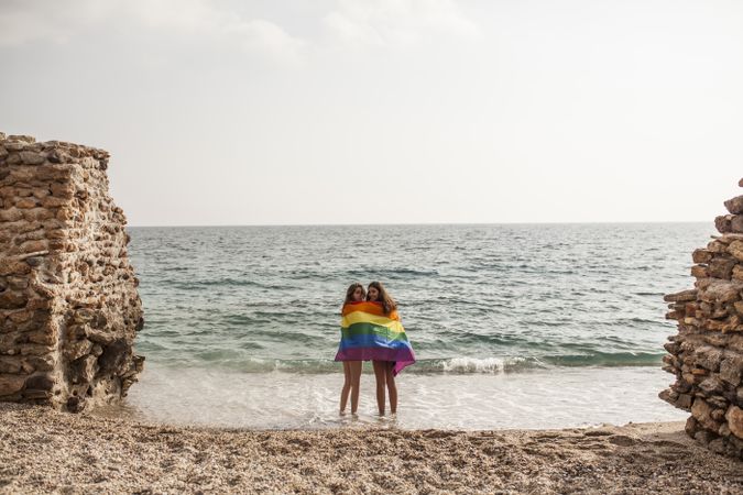 Females standing with rainbow flag on seashore