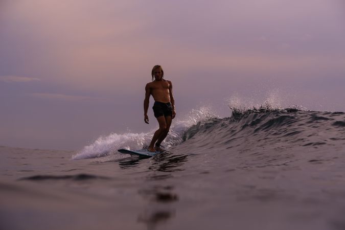 Man on surf board on waving water at sunset