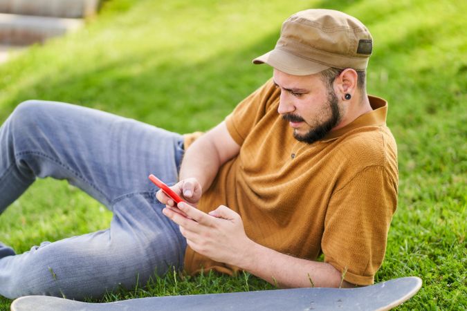 Relaxed man lying on the grass using the phone