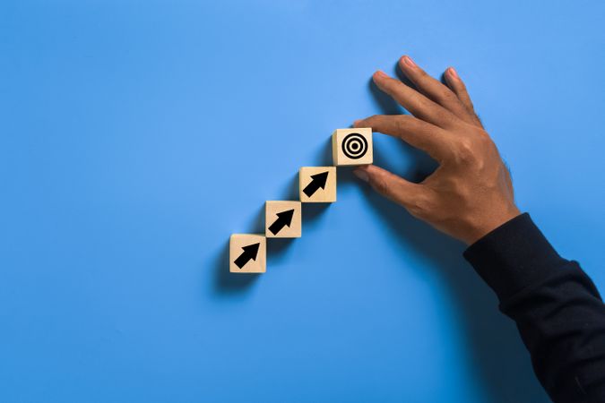 male hand put arrow up and target on wooden blocks isolated on blue background. concept of goals achievement