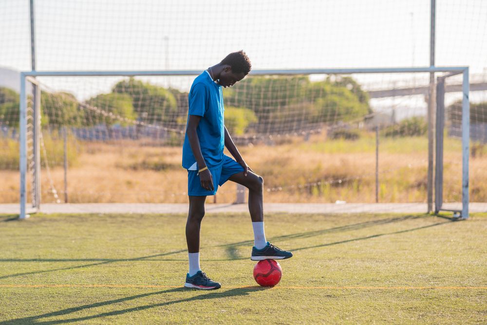 Black football player with ball standing on stadium