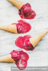 Four cones of dark berry ice cream melting on marble slab bGE1e5