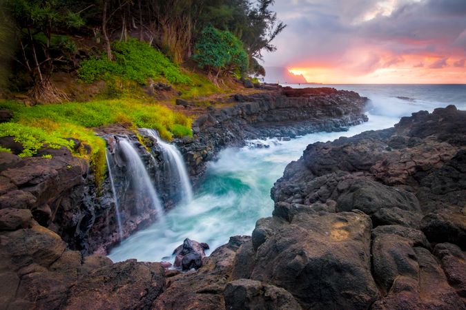 Waterfall on rocky shore during sunset